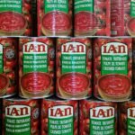 Close-up of stacked cans of crushed tomatoes in vibrant red with multilingual labels.