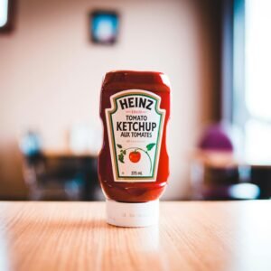 A Heinz Tomato Ketchup bottle on a wooden table with blurred background indoors.
