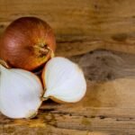 Detailed view of a whole and sliced onion on a textured wooden surface.