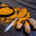 Vibrant turmeric powder and root on a dark wooden surface, emphasizing natural spices.
