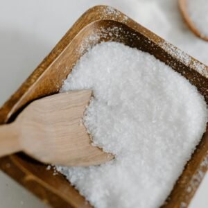 Close-up of coarse sea salt in a wooden bowl with a wooden scoop, perfect for culinary use.