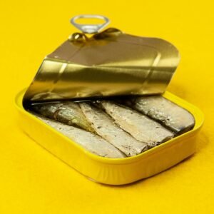 Close-up of an open sardine can on a vibrant yellow background, suitable for ads.