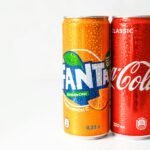 Close-up image of refreshing Coca-Cola and Fanta cans with water droplets.