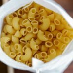 Overhead view of uncooked pasta in a white sack, emphasizing food and sustainability.