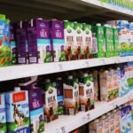 Various milk cartons displayed on shelves in a bright supermarket aisle.